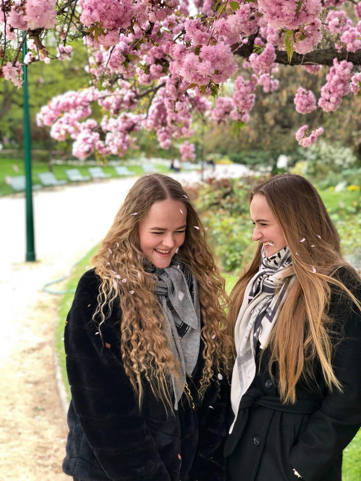 To unge kvinder griner under et blomstrende kirsebærtræ